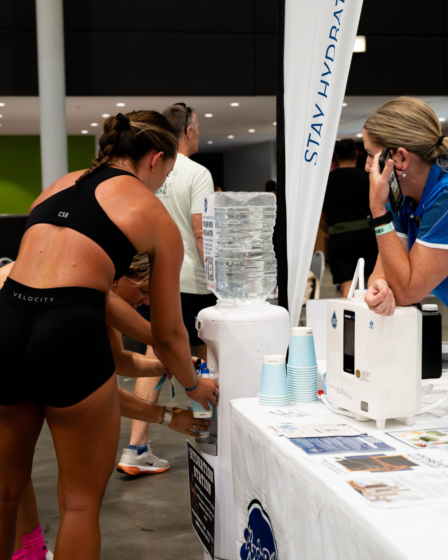 An athlete fills her bottle at the Hydr8tion N8tion hydration station while a team member looks on