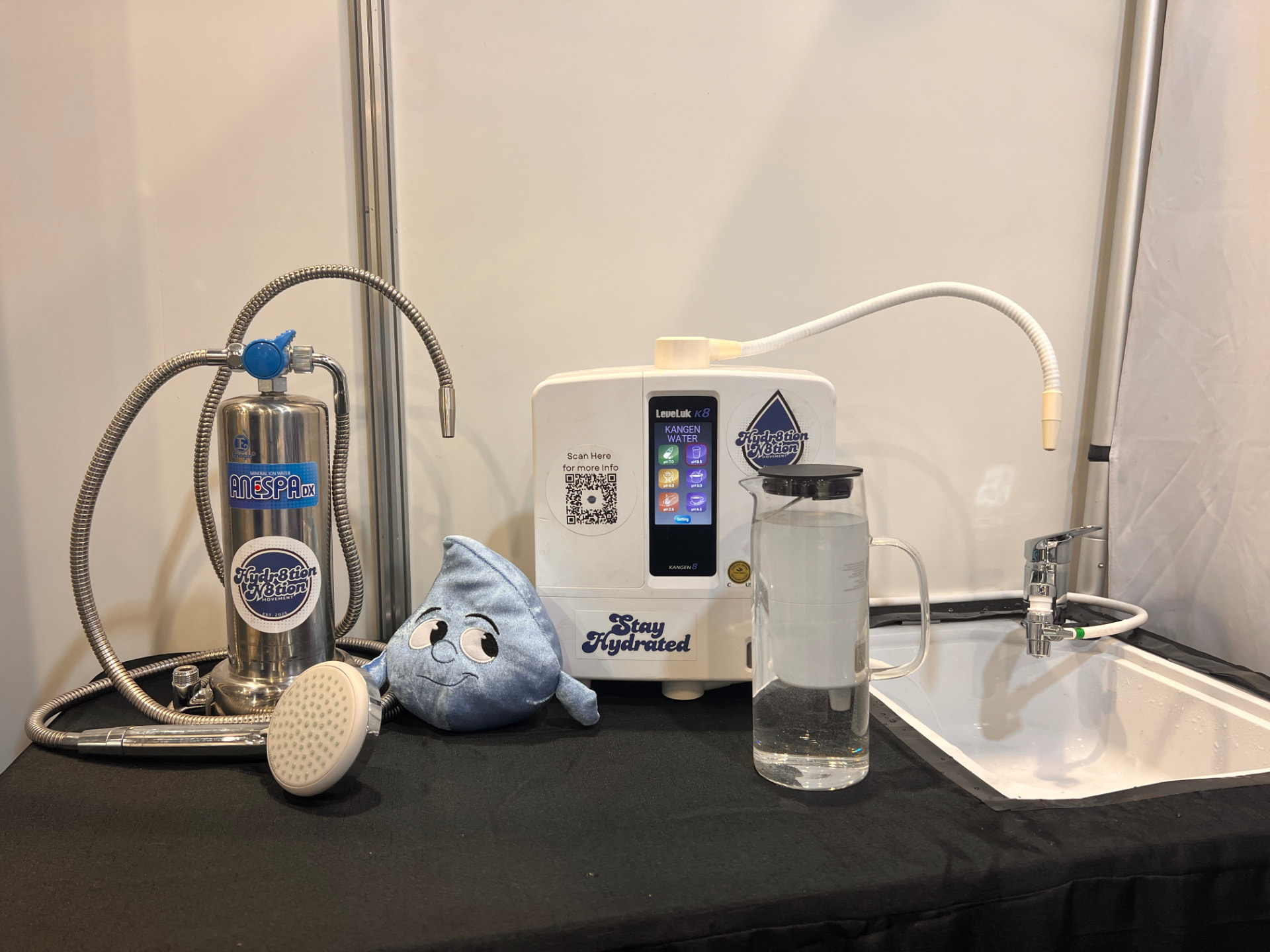 Kangen K8 and Anespa DX systems with a water jug and sink on the Hydr8tion N8tion stand